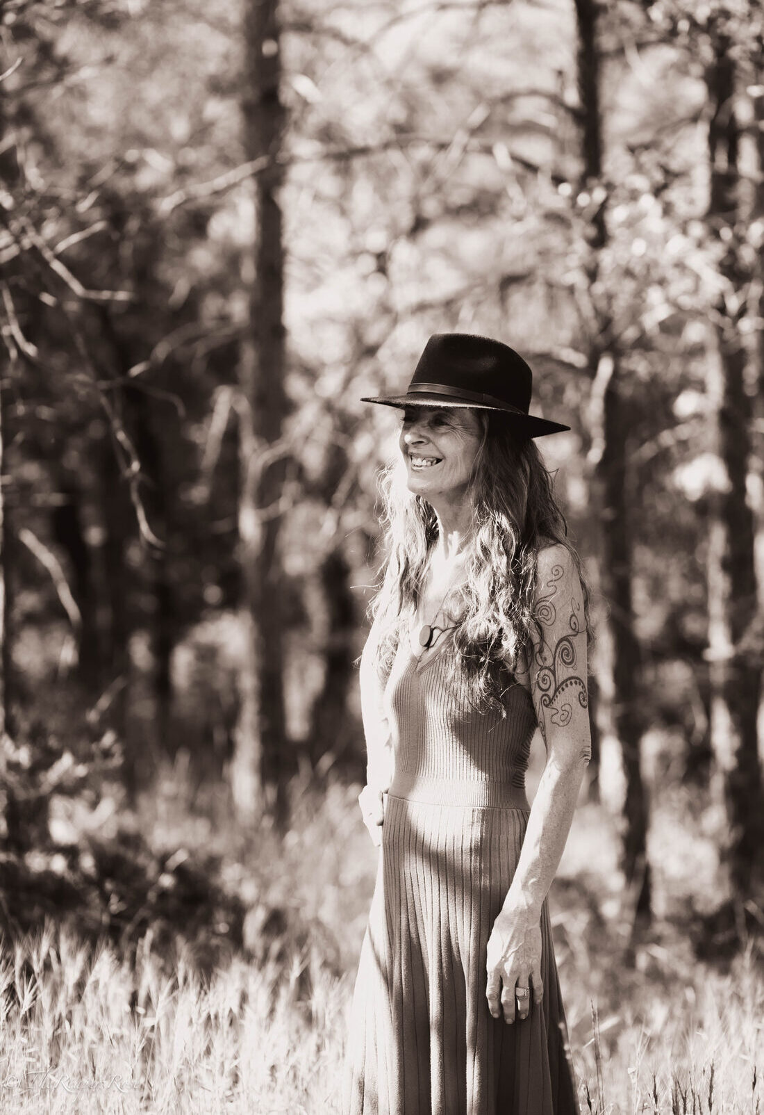 Fiona Gardner in a wide-brimmed hat, smiling in a sunlit pine forest